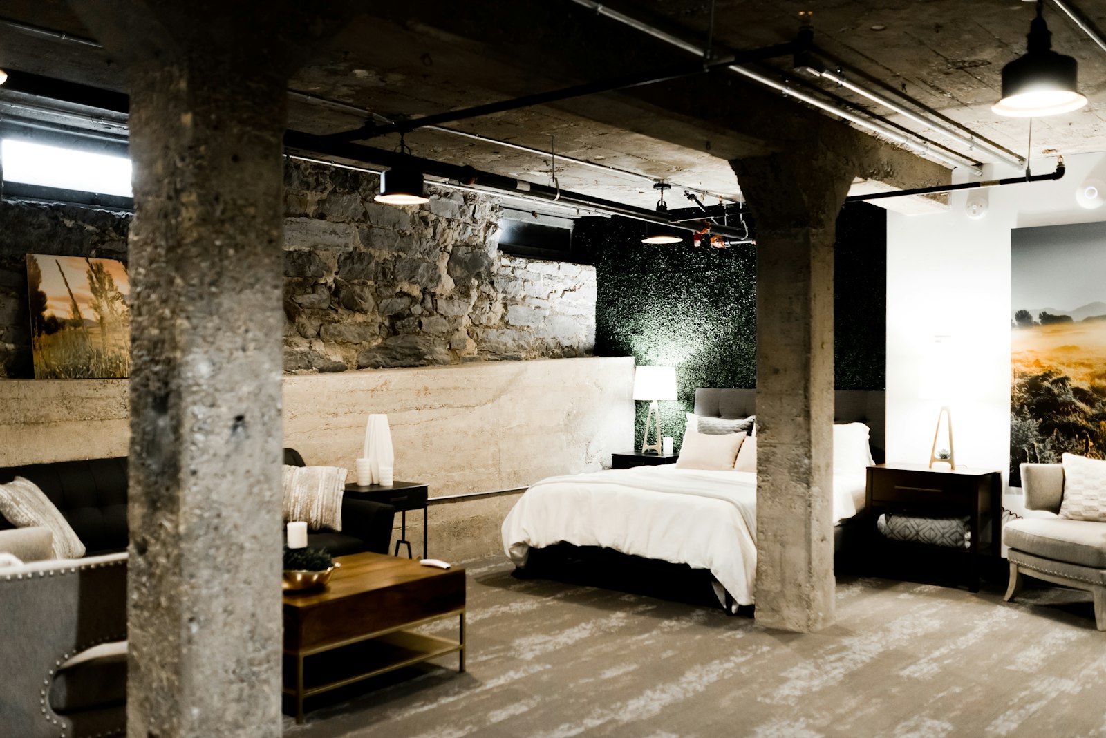 A boutique hotel room with exposed stone and concrete walls, crisp white linen and warm lamplight at dusk