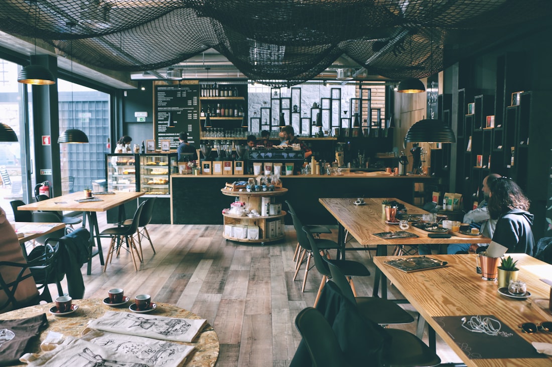 A warm café-lounge with hanging lights and timber tables, a guest seated reading by the window