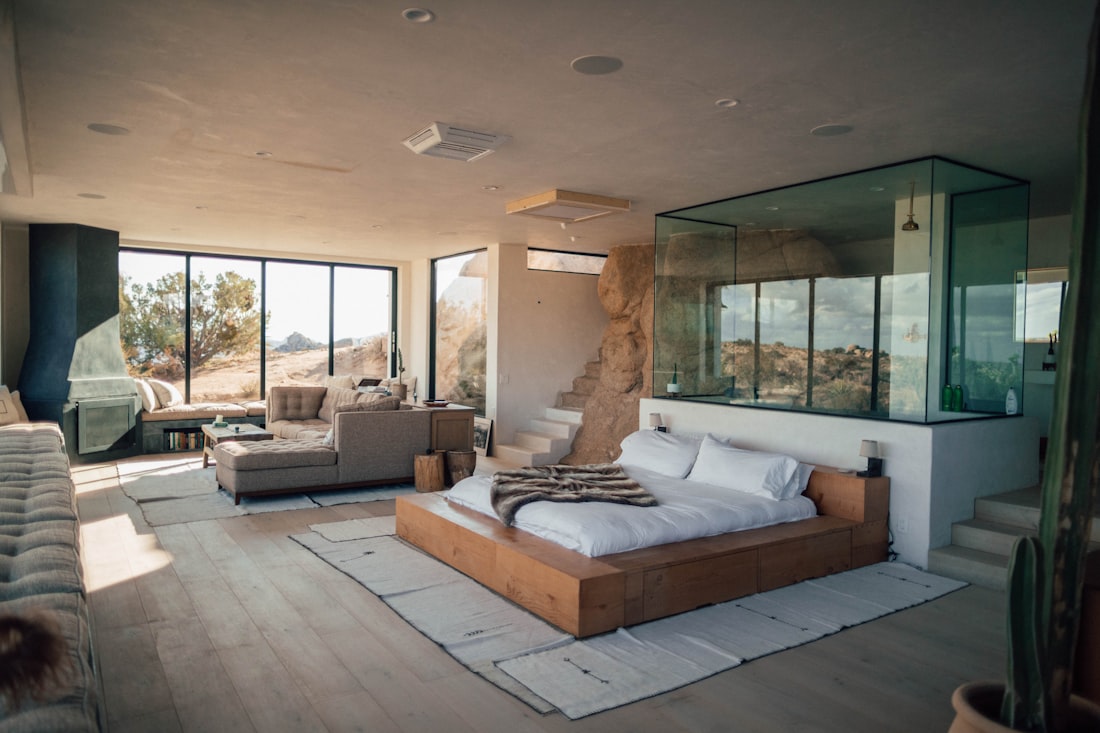 A calm bedroom with floor-to-ceiling windows opening to morning light, linen and timber tones